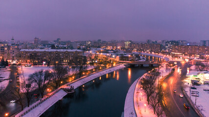 Illuminated evening riverbank with lights reflection in dark water near Skver Strilka in Kharkiv city center. Winter aerial colorful color graded photo