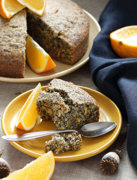 Poppy seed and orange peel vegan egg free and dairy free cake, bite on the orange plate with blue linen textile and poppy head nearby, closeup, copy space, vegan food and pastry concept