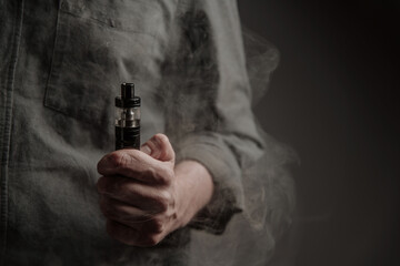 vape in man hand on gray background. There is a lot of smoke around