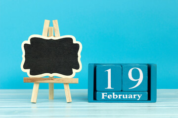 wooden calendar with the date of February 19 and an easel on a blue background, place for text,...