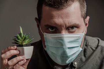 man in a medical mask with a small green plant in a pot looking at the camera