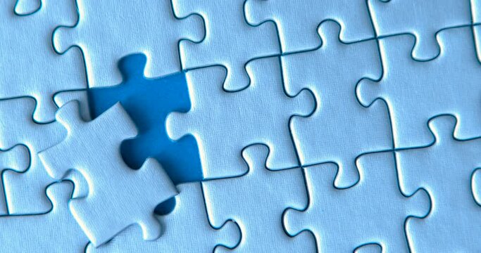 Gray puzzles stacked on blue background. Female hand is putting down one piece. Finishing, completion of work task. Successful achievement of goal. Decision, solution of problem, issue found.