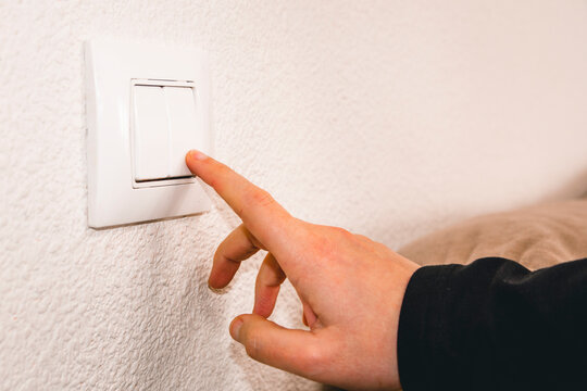 Close-up of a hand turning off a light switch. Concept of energy saving at home.