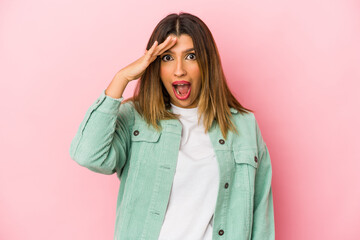 Young indian woman isolated on pink background shouts loud, keeps eyes opened and hands tense.