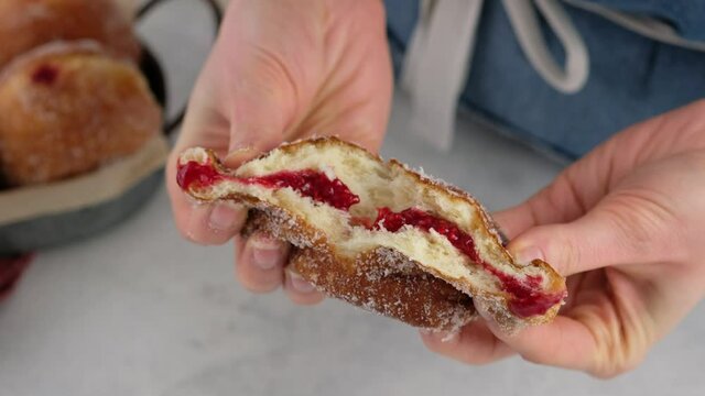 Berliners. Close-up female hands breaking a donut with raspberry jam on a white background, a cutaway donut with a filling filling. Delicious sweet donut. Making donuts with jam.
