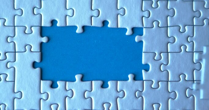 Gray puzzles stacked on blue canvas background. Female hand is putting down pieces. Finishing, completion of work task. Successful achievement of goal. Decision, solution of problem, issue found.