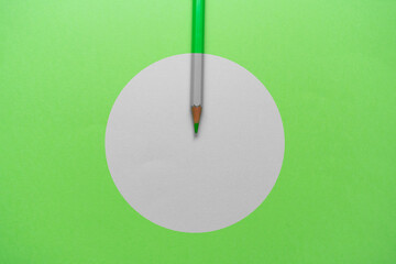 Green pencil over a green background, with a white circle in the middle.