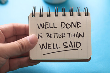 Well done is better than well said, text words typography written on book against blue background,...