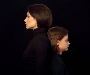 Beautiful concentrated serious mother and her angry emotional thinking daughter standing back to...