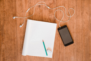 Pencil, eraser, notebook, cell phone and headphones on wooden table in daylight
