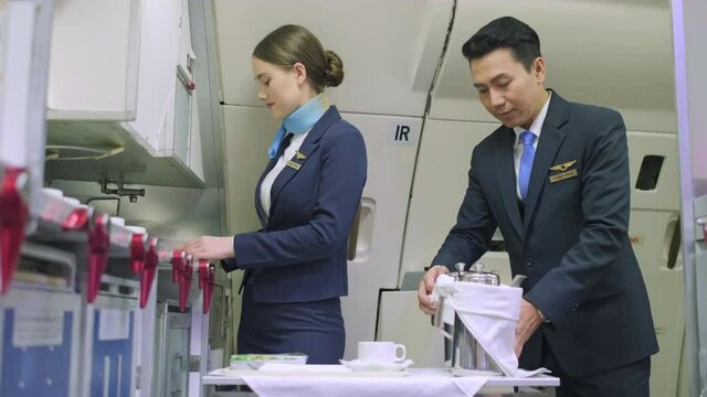 Flight attendance in uniform in the first class of airplane, preparing food and drink for passenger. Staff check the quality of food and prepare tea and coffee. Travel and service concept.