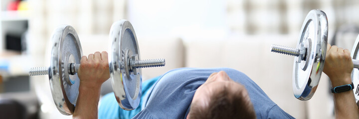 A man at home raises heavy dumbbells from a prone position. Interval and cardio training for burning fat