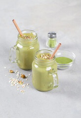 Energy drink smoothie made with oatmeal, walnuts and green matcha tea in a glass jar with bamboo straws on a light gray background