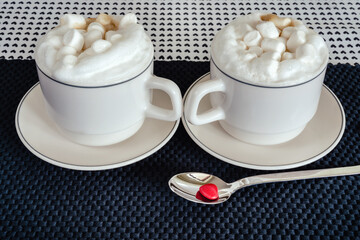 Two cups of cappuccino or latte with marshmallow. Love coffee for Valentines date. Lovely hearts shape pattern on background napkin.