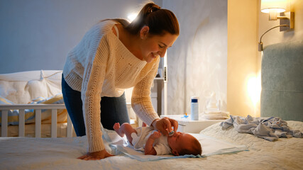Young caring mother giving soother to her little baby boy crying on bed at night. Parent giving...