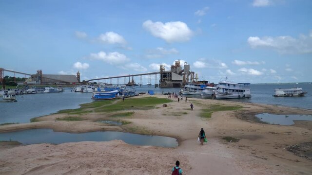 Beautiful view of Tapaj&oacute;s river landscape, people walking on sand riverside, traditional boats and port in the background on sunny summer day in the Amazon. Cityscape of Santar&eacute;m, Par&aacute;, Brazil. 4K