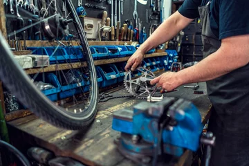 Schilderijen op glas Vintage bicycle repair workshop. Man fixing bicycle parts with a wrench working in garage, service in auto repair station. Bicycle repairing. © Vladimir Borovic