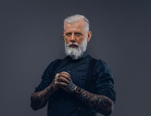 Trendy and confident grandfather with tattooed hands dressed in modern clothing poses in dark background.