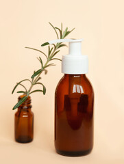 Brown glass bottle with a pump of cosmetic products framed by green leaf branches, beige background. Natural organic spa cosmetic beauty concept. Front view Mock up.