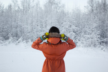 Woman wearing orange hooded coat and yellow mittens with deers walks in a winter forest. People from behind. Snowy forest background. Winter traveling lovers concept. © Intergalactic Rada