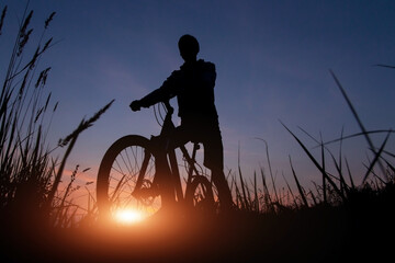 Fototapeta na wymiar Silhouette of a cyclist against the sunset sky with sun and sunlight, copy space