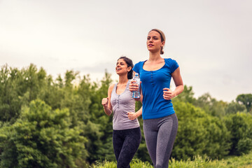 Two beautiful young fitness women running outdoors. Two fit female jogging