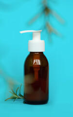 Brown glass bottle with a pump of cosmetic products framed by green leaf branches, blue background. Natural organic spa cosmetic beauty concept. Front view Mock up.