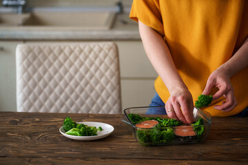 Close-up, a woman prepares a dish of red fish, salmon and broccoli in kitchen