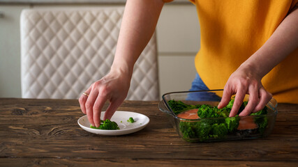 Close-up, a woman prepares a dish of red fish, salmon and broccoli in kitchen