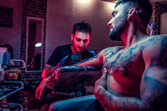 Tattoo artist in black gloves making a tattoo on the arm of man