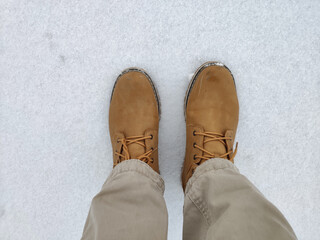 Top down view of pants and pair of brown winter boots in white snow