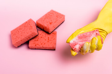 Top view of hand in rubbed glove holding sponge with soapsuds near sponges blurred on pink background