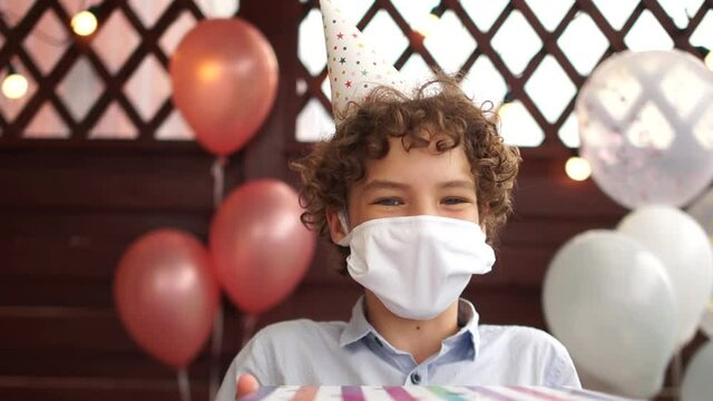 Happy birthday boy wearing protective mask, close-up portrait. Masked boy holding gifts boxes in his hands, stay home, new normality
