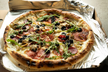 Close-up of pizza with olives, salami, rucola and cheese in a box. Delivery of orders from the restaurant.