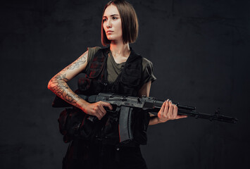 Dressed in dark armour military woman with short haircut and bandaged hand holds her assault rifle in dark smokey background.