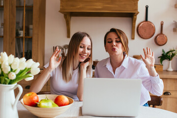Smiling hipster girl talking and waving hand hello during online video call via laptop computer,...