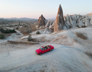 The pink retro cabriolet car is standing alone on the hills valley background on. A nice place for a romantic date. Top view aerial drone landscape, Cappadocia, Turkey. Saint Valentine's Day concept.