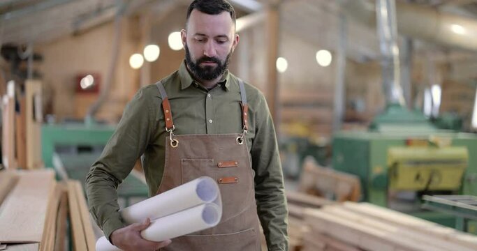 Portrait of a handsome carpentry worker, taking some blueprints in the joinery manufacturing. Craftsman designing woodwork