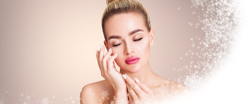 Young beautiful woman over beige background with snow and snowflakes. Cryolifting concept.
