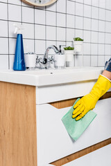 Cropped view of woman cleaning side of sink with rag near detergent in bathroom