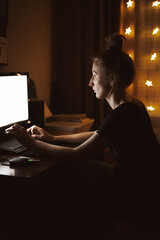 Young woman working late at night at the computer in home interior. Top view of the girl typing. Remote work, night waking, working overtime, finding information.