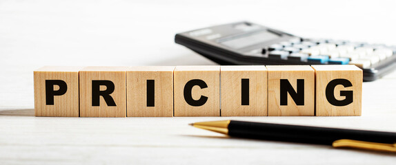 On a light background, a pen, calculator and wooden cubes with the inscription PRICING. Defocus