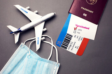 Traveling during COVID-19 virus, passport with airline ticket, covid-19 vaccinated card with "Yes" mark, medical mask and plane on grey background, airport security health and safety check concept