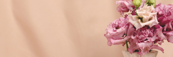 Banner with bouquet of eustoma flowers in front of beige cloth background. Springtime minimal composition with copyspace.