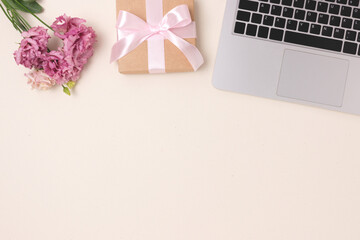 Laptop, bouquet of flowers and gift box with tied bow on a beige background. Online dating concept, present for Mothers or Valentines Day with copy space.
