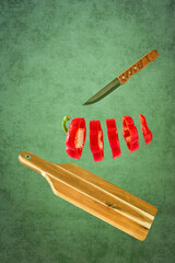 Ein in Scheiben geschnittener roter Paprika mit einem Messer und einem Schneidebrett vor einem grünen Hintergrund
