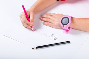 Kid draws with pencils. GPSwatch on child hands. Pink smart watch on hand.