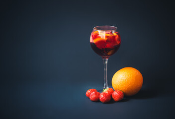 Red wine sangria with orange and strawberry in glass, orange and strawberry near. Dark background.