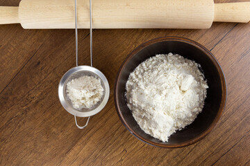 Flour in a wooden bowl, a small sieve and cinnamon sticks on a wooden table. Top view with copy space. Kitchen baking tools with place for text, or logo.