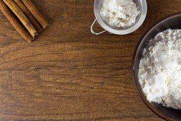 Flour in a wooden bowl, a small sieve and cinnamon sticks on a wooden table. Top view with copy space. Kitchen baking tools with place for text, or logo.